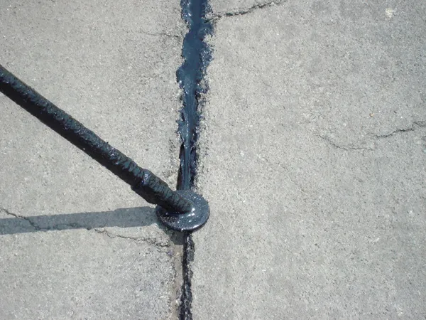 Close-up of hot rubber sealant filling intersecting asphalt cracks